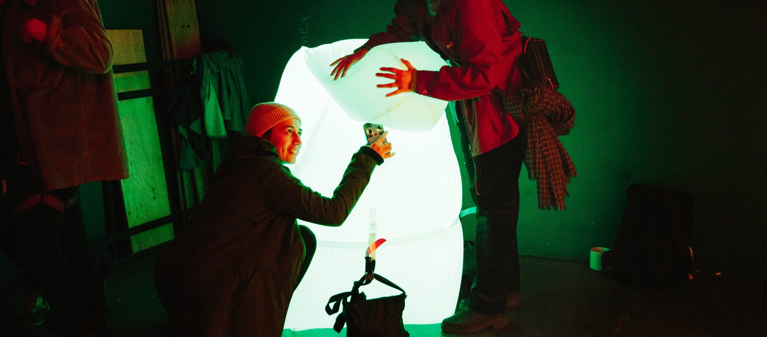 People embracing a large, glowing, inflatable art installation with a pale green hue.