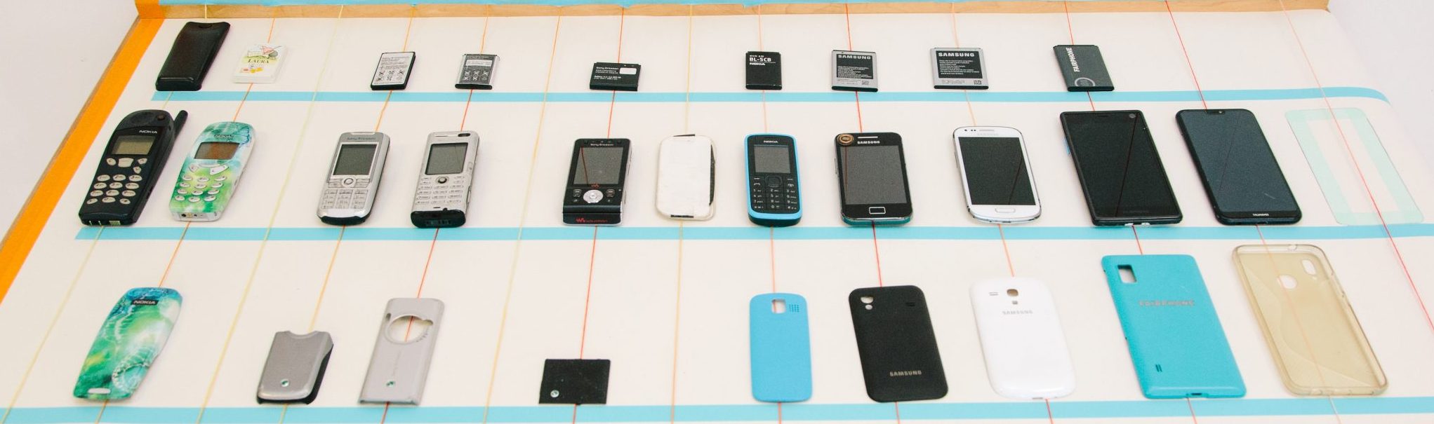 A desk showing an array of old and new mobile phones and phone cases ordered neatly