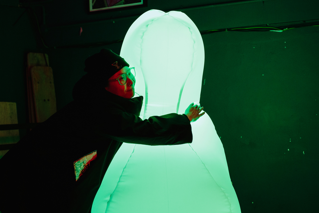 A person embracing a large, glowing, inflatable art installation with a pale green hue.