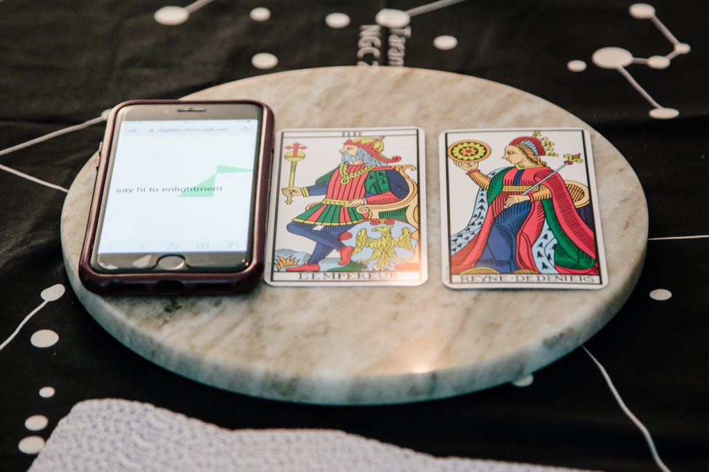 A phone which reads 'say hi to enlightenment' next to two traditional tarot cards: empereur and reyne de denier