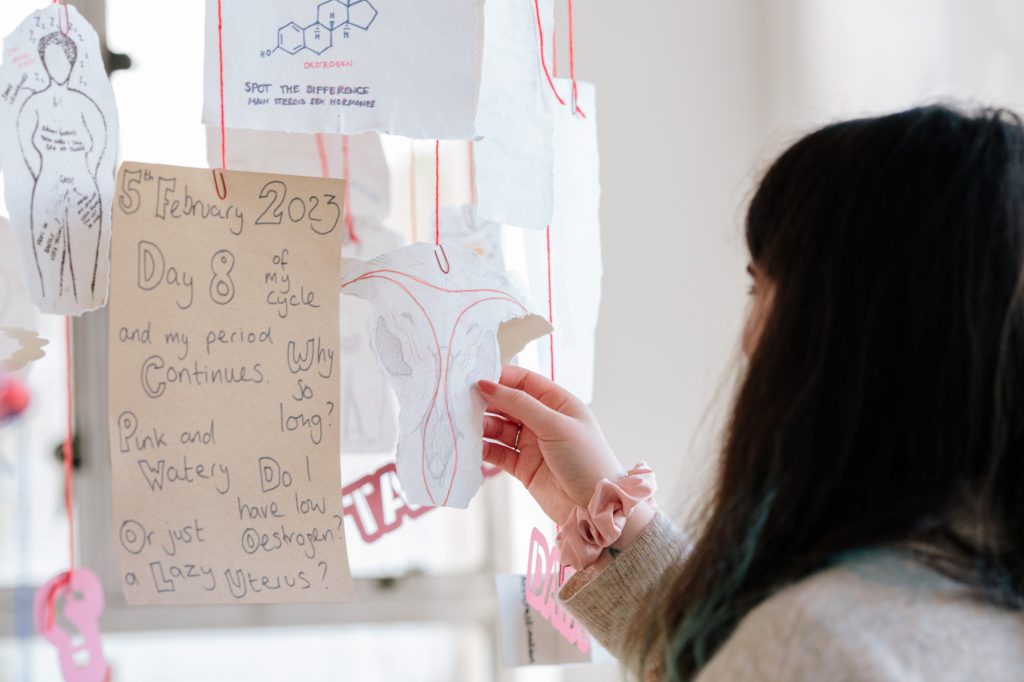 A person holding a piece of paper with a drawing of a utreus on it. It is hanging from red string alongside other paper hanging from red string.