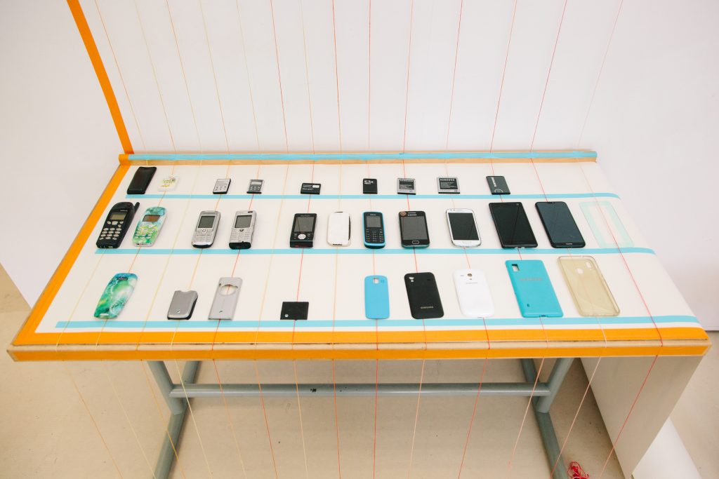 A desk showing an array of old and new mobile phones and phone cases ordered neatly