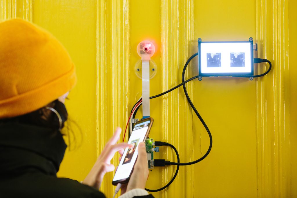 A person touching a photo of the mona lisa on their phone, which is wired to a screen attached to a yellow door.