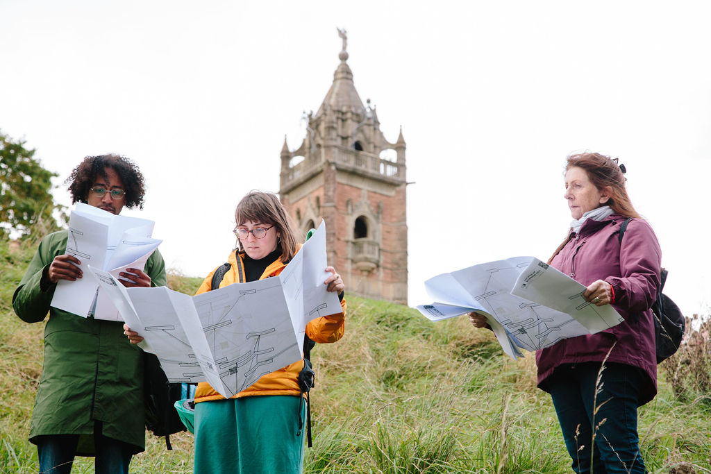 People holding large pieces of paper in a green space with a tower in the background.