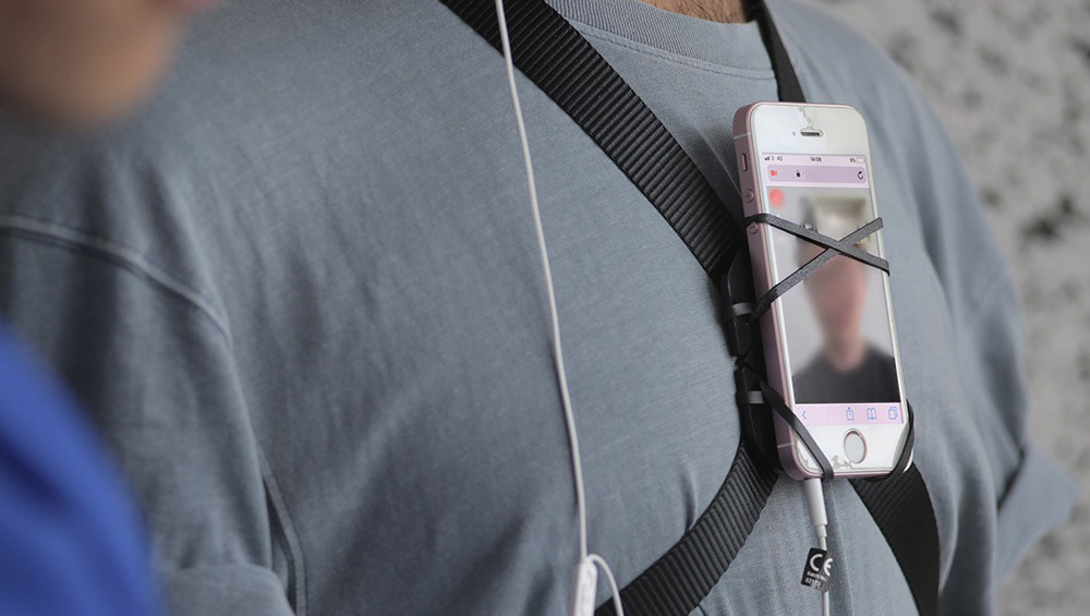 A phone screen strapped to a person's chest using black fabric and elastic bands.