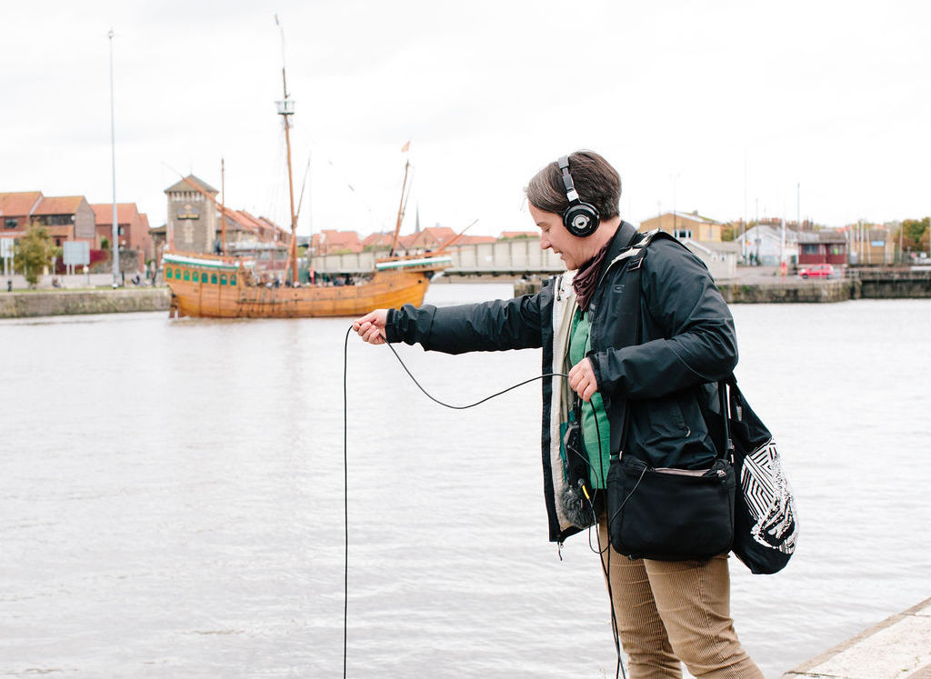 A person wearing headphones dangling a wire into the river.