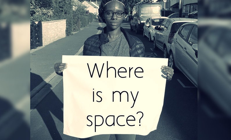 A person stood in the middle of a residential-looking street holding a white piece of paper which has digital text reading 'where is my space?'